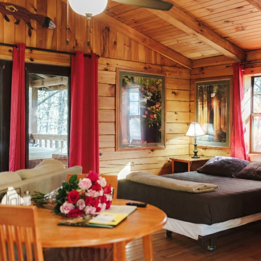 Cozy wooden cabin interior with a bed, a dining table, and floral decor.