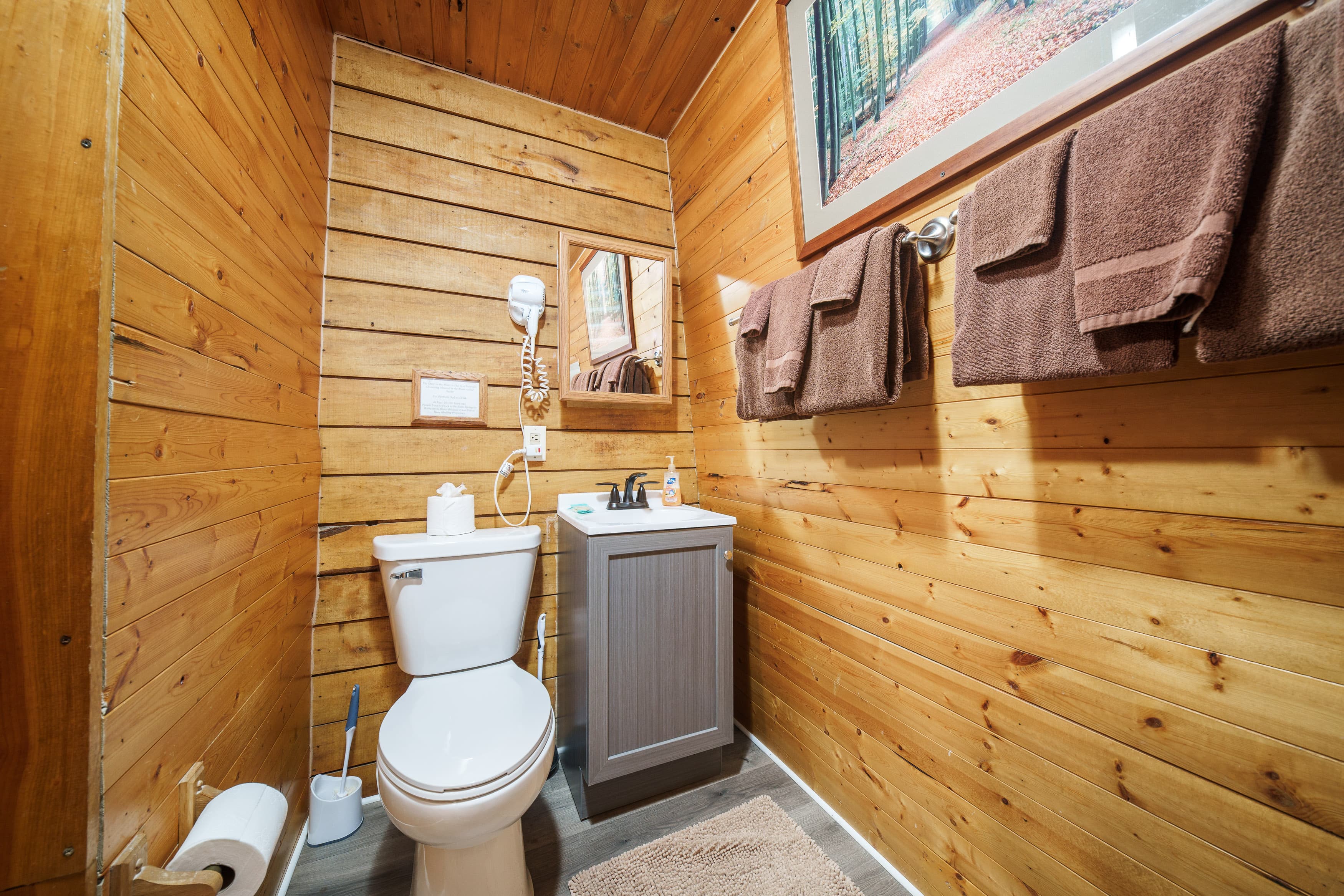 A cozy wooden bathroom featuring a toilet, sink, and brown towels.