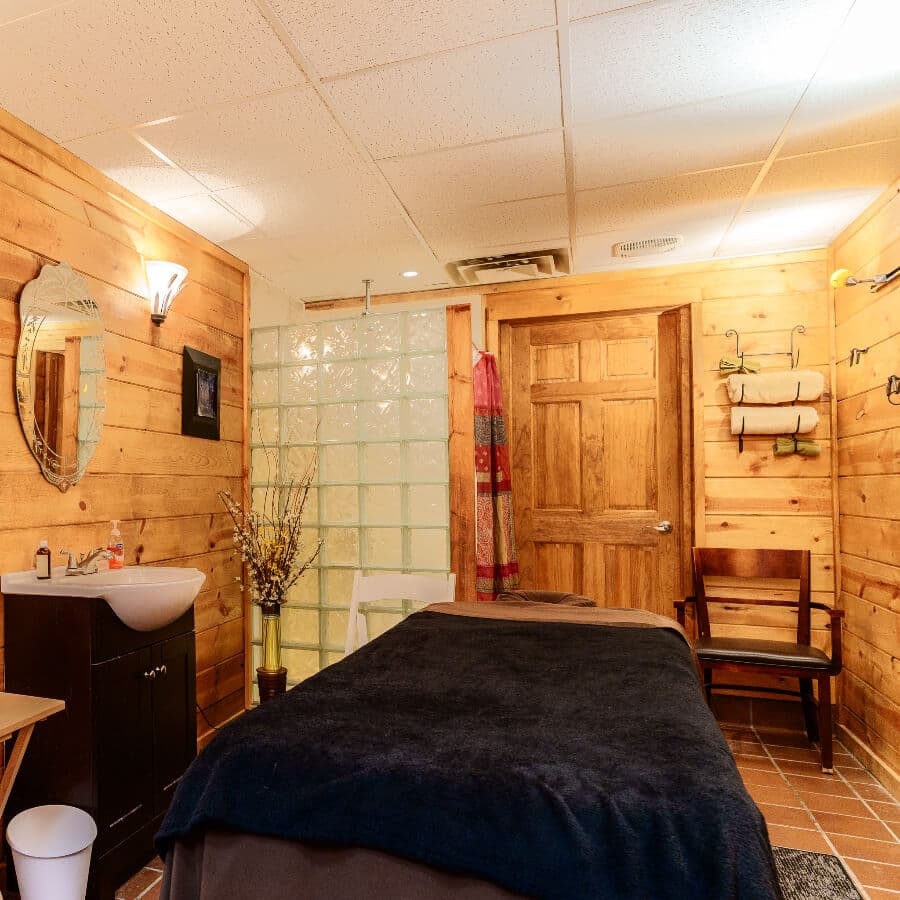 A serene spa room featuring wooden walls, a massage table, and a shower area.