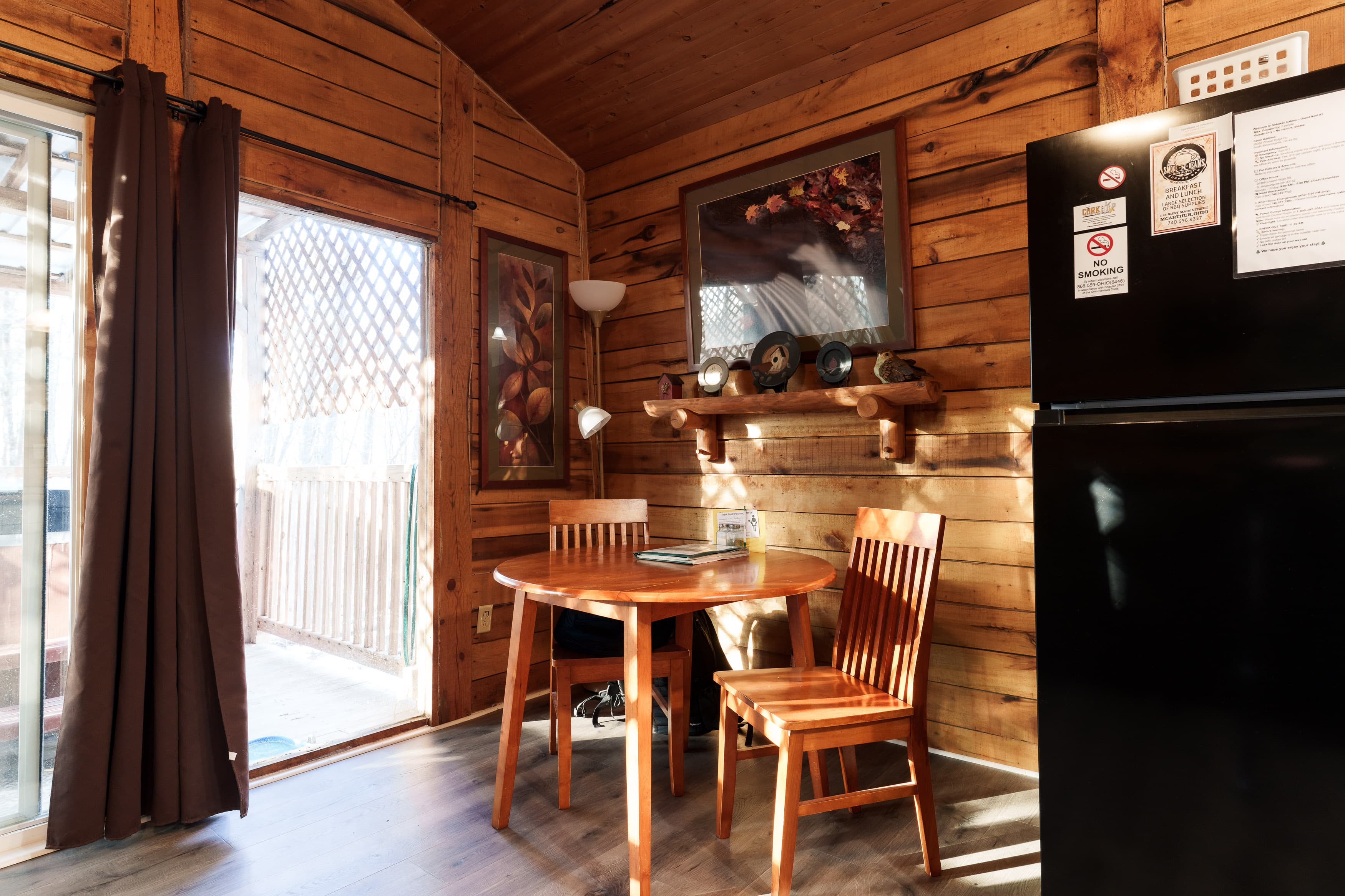 Cozy wooden cabin interior featuring a round table with two chairs and a refrigerator.