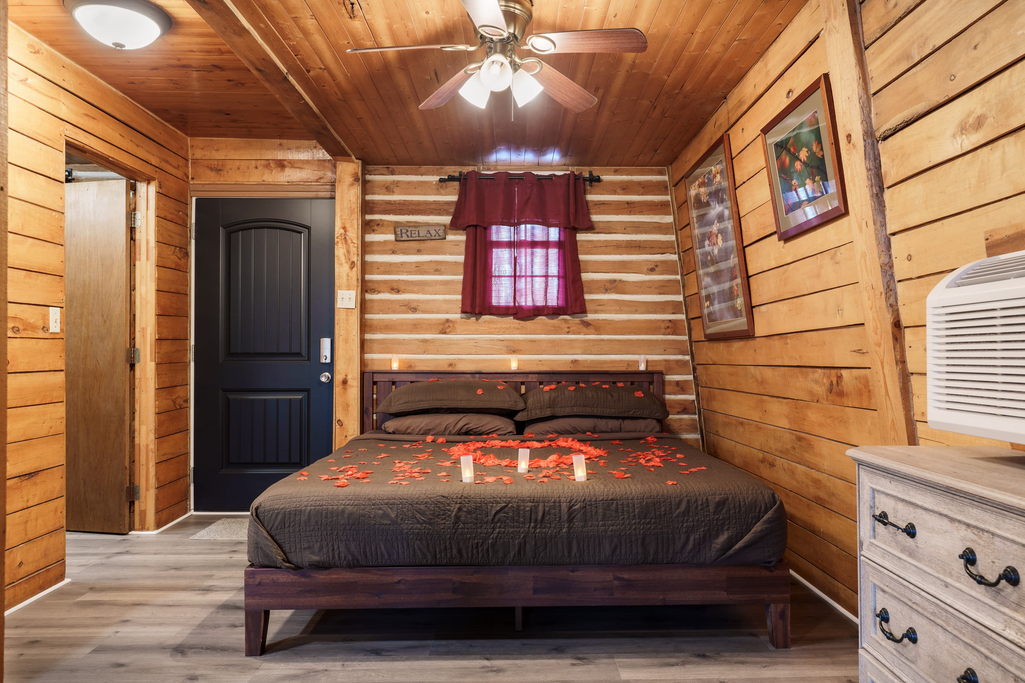 Cozy wooden bedroom featuring a double bed adorned with red petals and rustic decor.