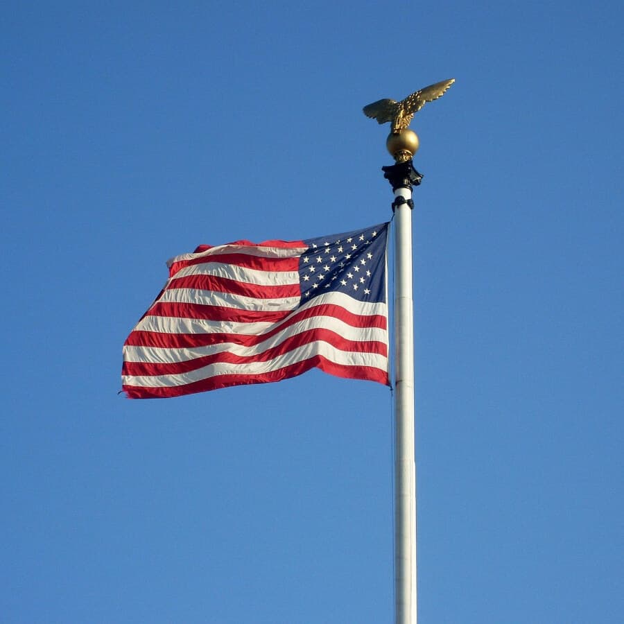 A United States flag waves atop a flagpole with a golden eagle ornament.