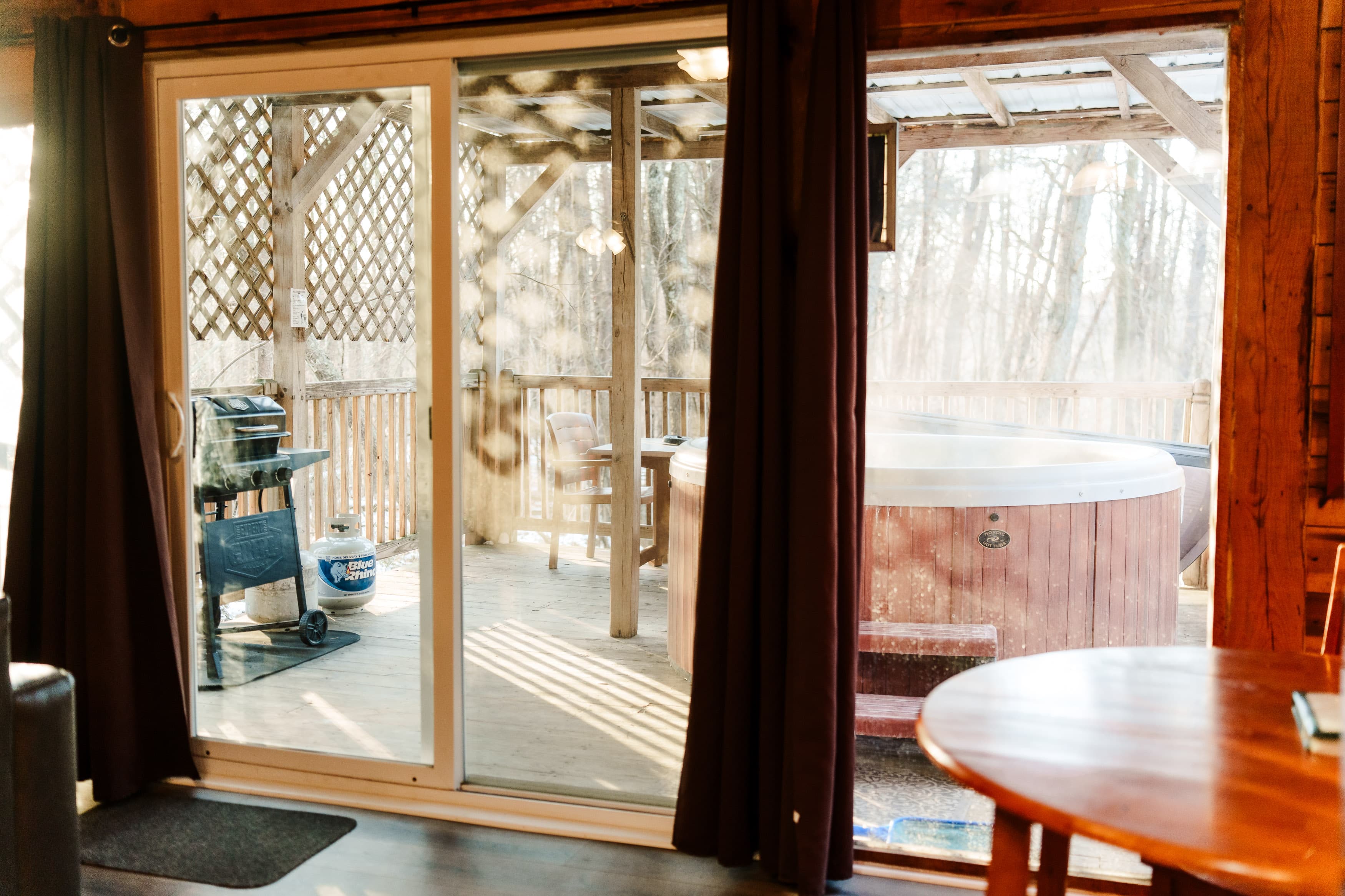 A view through a glass door into a wooden deck with a hot tub and grill.