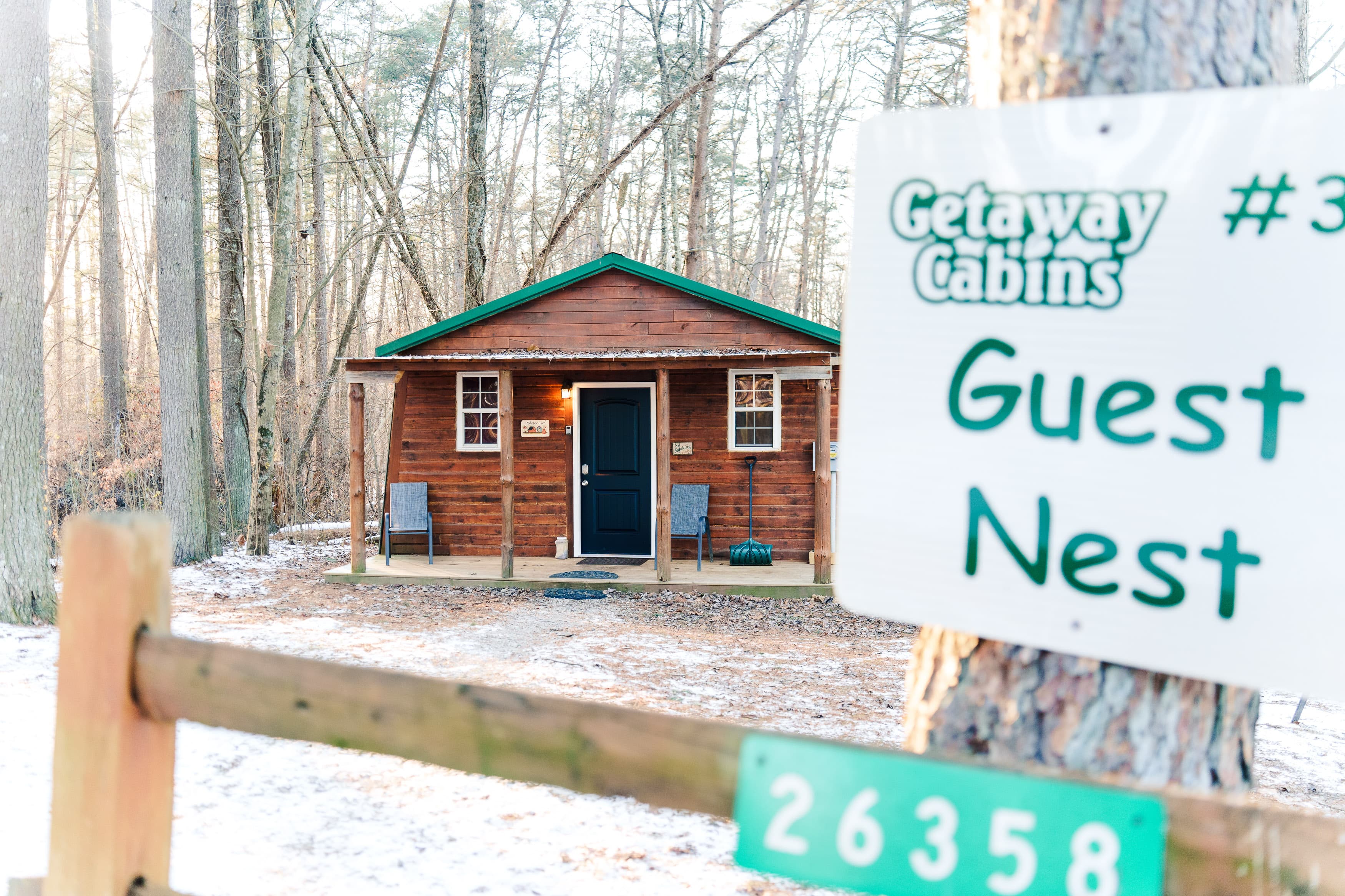 A cozy wooden cabin with a green roof, surrounded by trees, featuring a sign that reads "Guest Nest."
