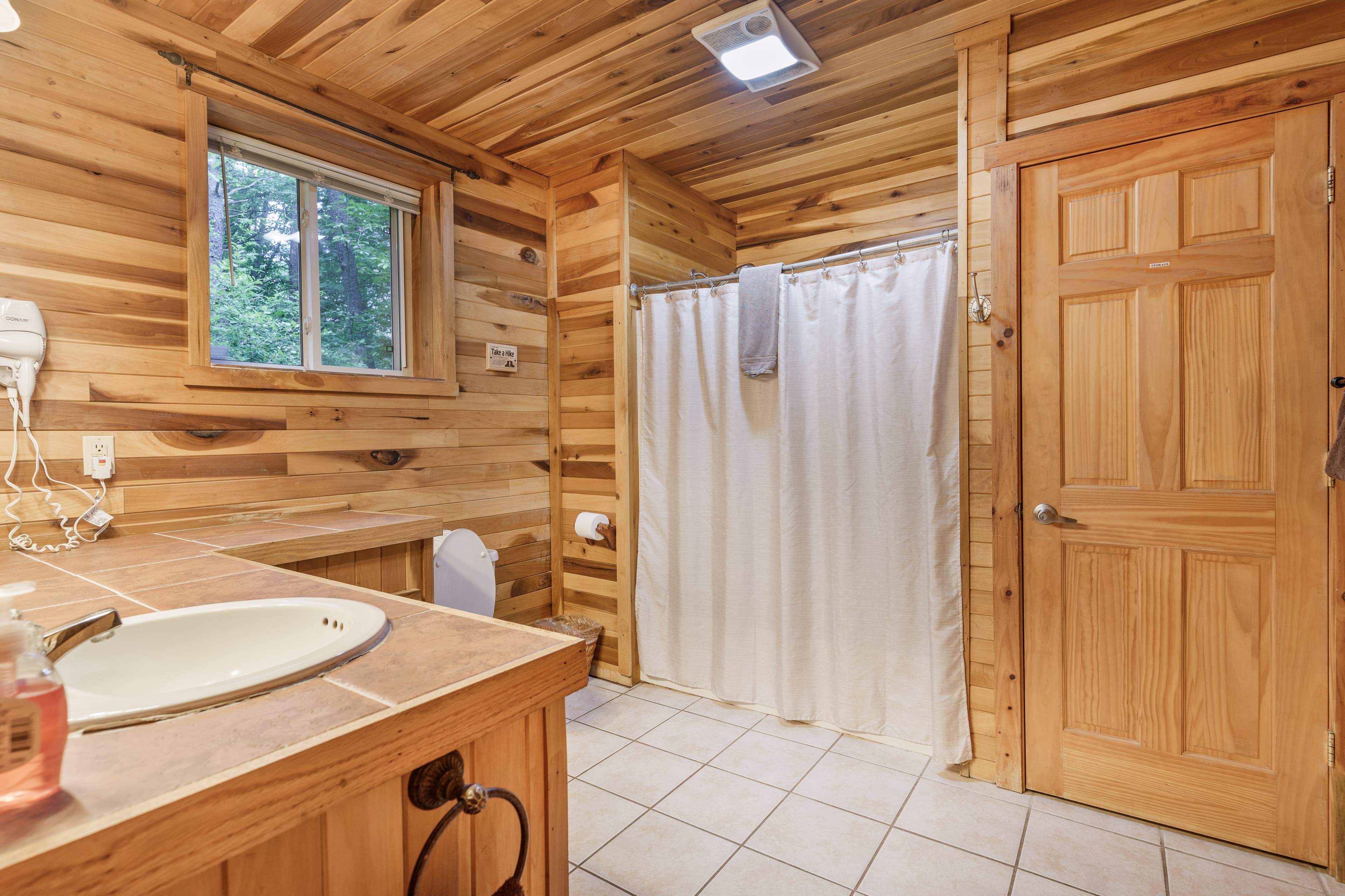 A bathroom interior showing a shower with a white curtain, a wooden door, and the edge of a vanity sink against pine walls.