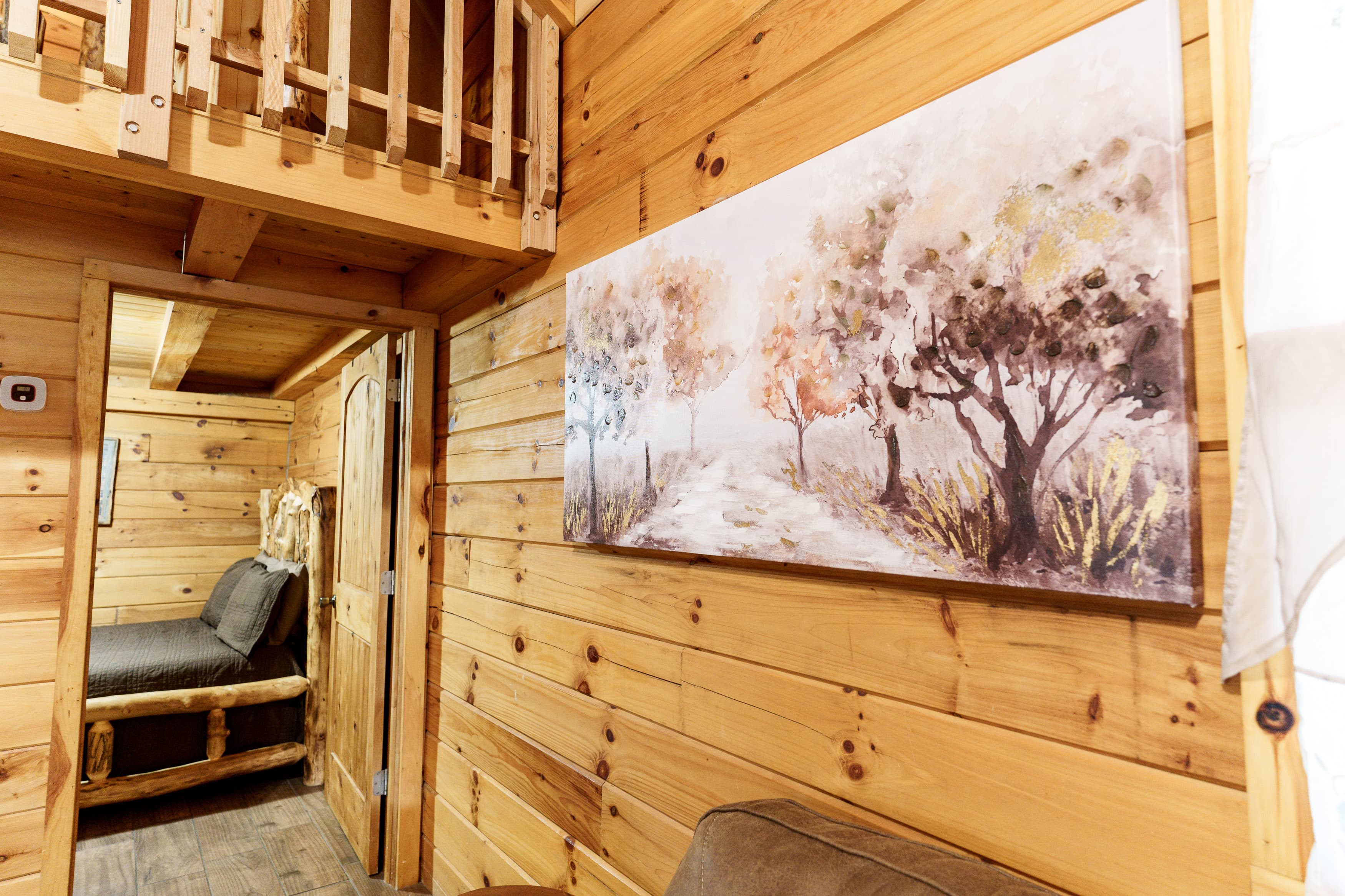Interior of a wooden cabin featuring a landscape painting and a view of a cozy seating area.