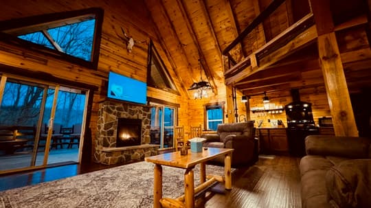 Cozy wooden cabin interior with a fireplace, large windows, and a modern TV.