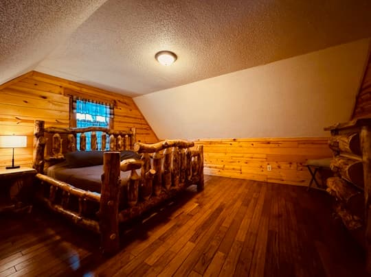 Cozy bedroom featuring a rustic log bed and wooden walls.
