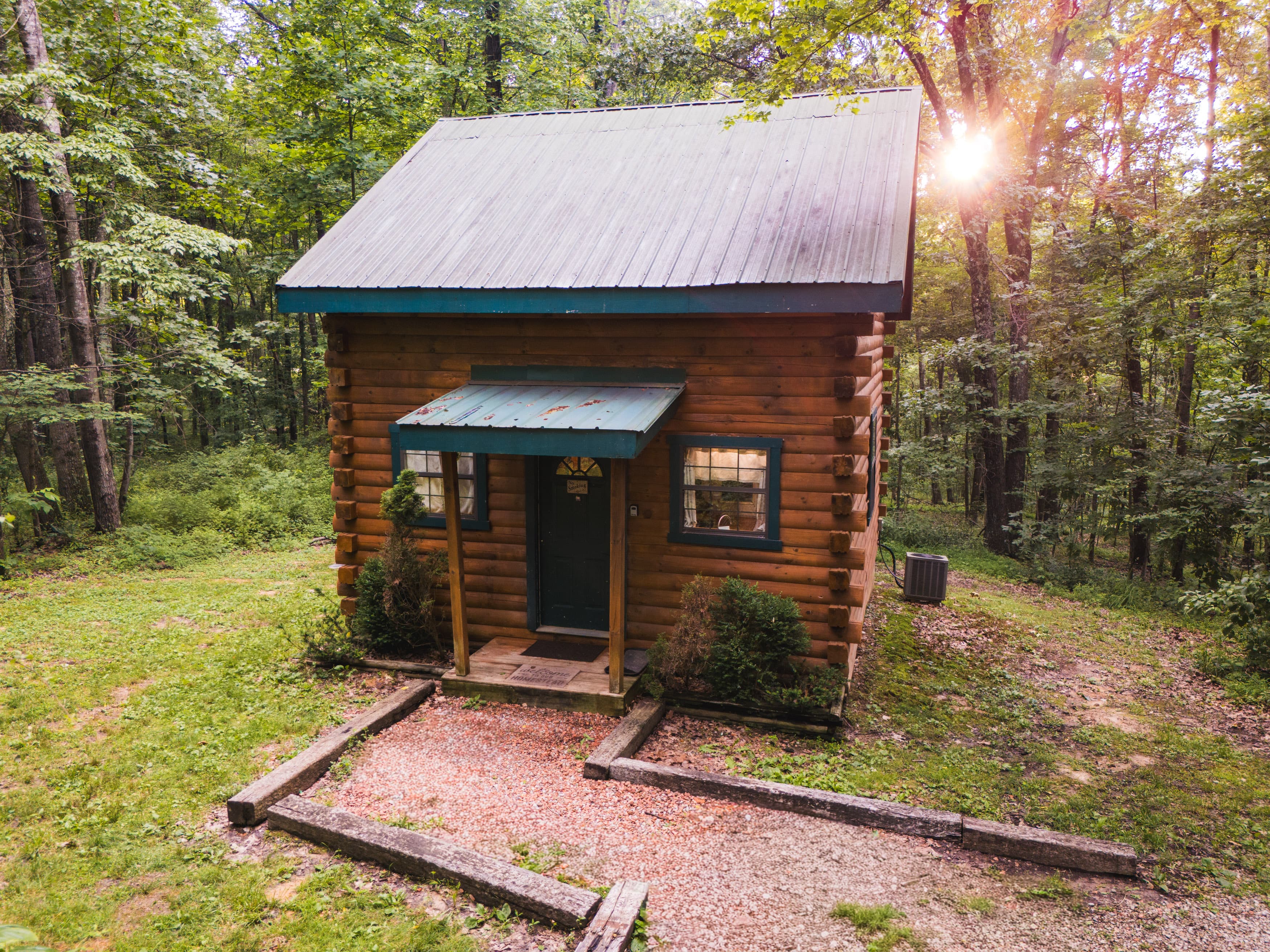 A rustic log cabin nestled in a wooded area, with sunlight filtering through the trees.