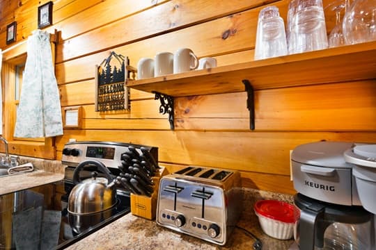 A cozy kitchen with wooden walls featuring a stove, kettle, toaster, and coffee maker.