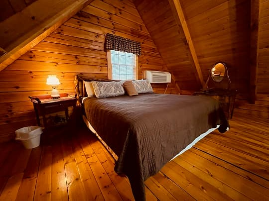 Cozy wooden attic bedroom with a brown quilted bed, small nightstand, and a window.