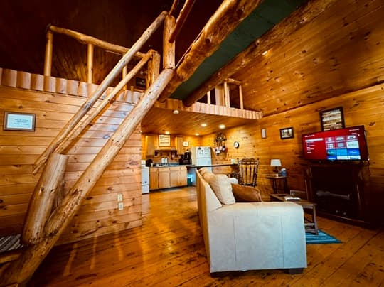 Cozy wooden cabin interior featuring a sitting area, staircase, and kitchen.