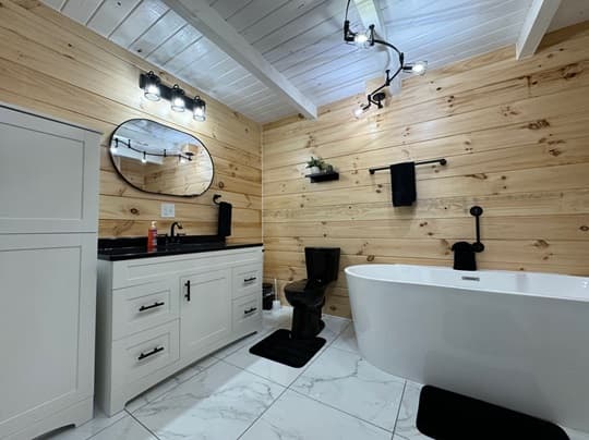 A modern bathroom with wooden walls, a freestanding tub, a black vanity, and stylish lighting.