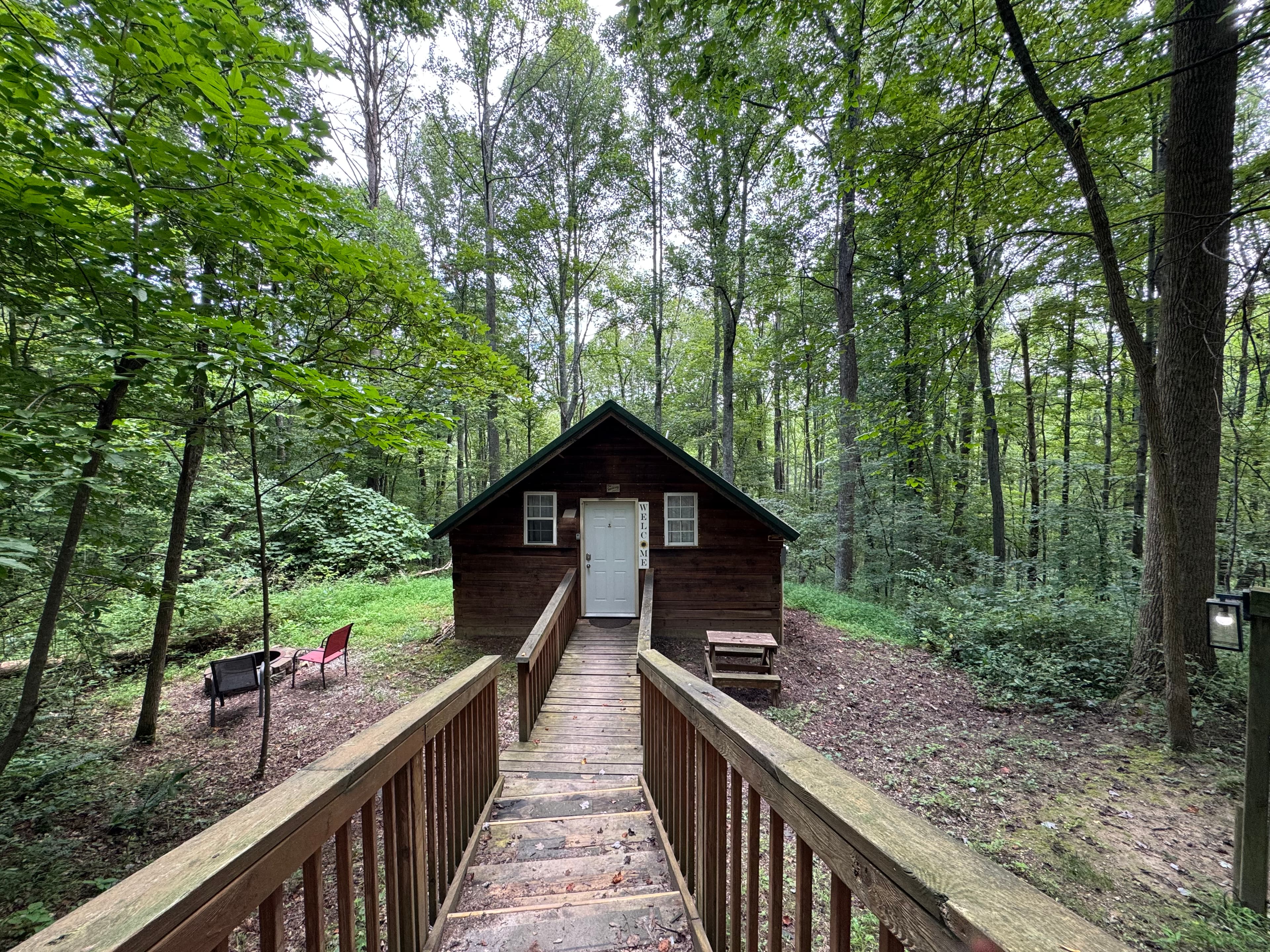 A wooden cabin surrounded by trees, accessed by a staircase with seating nearby.