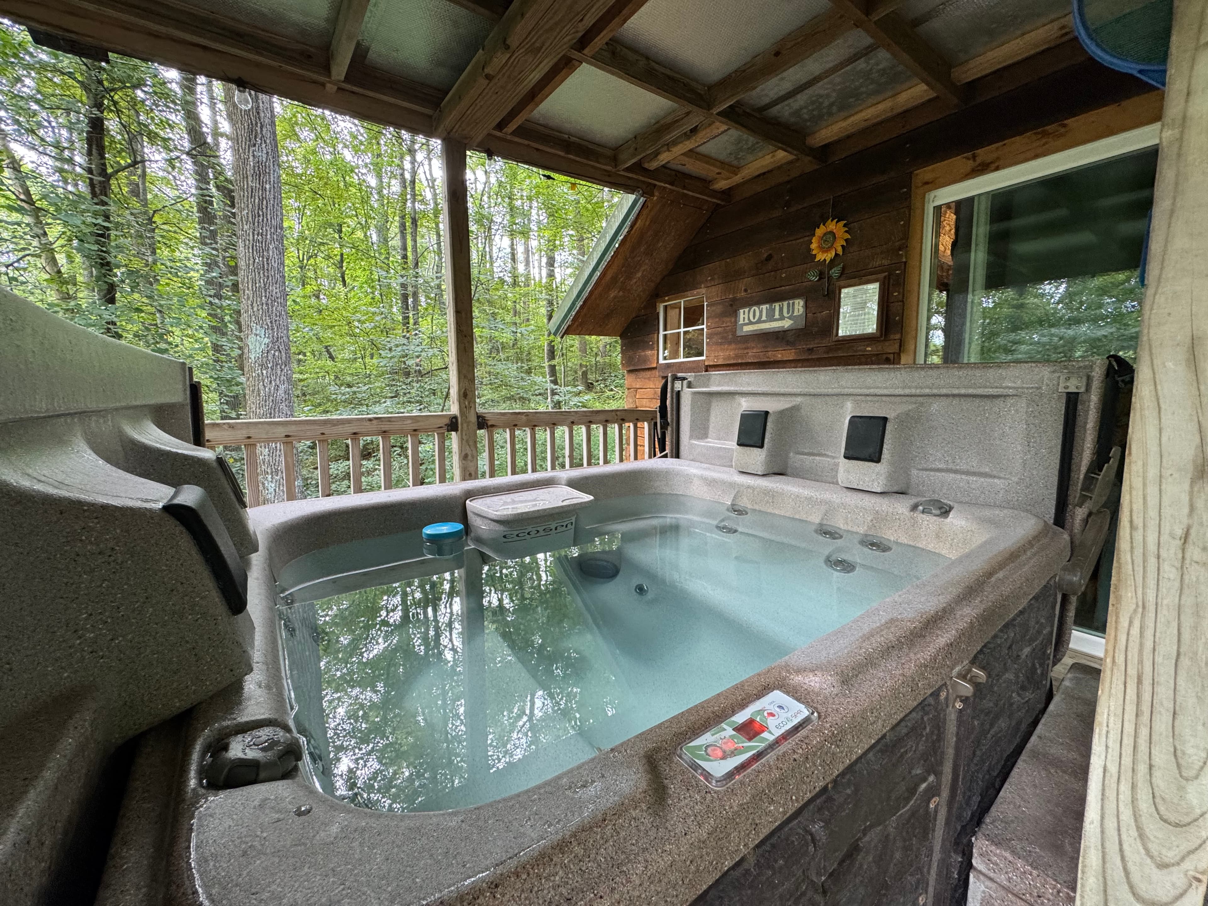 A hot tub surrounded by trees on a cabin deck.