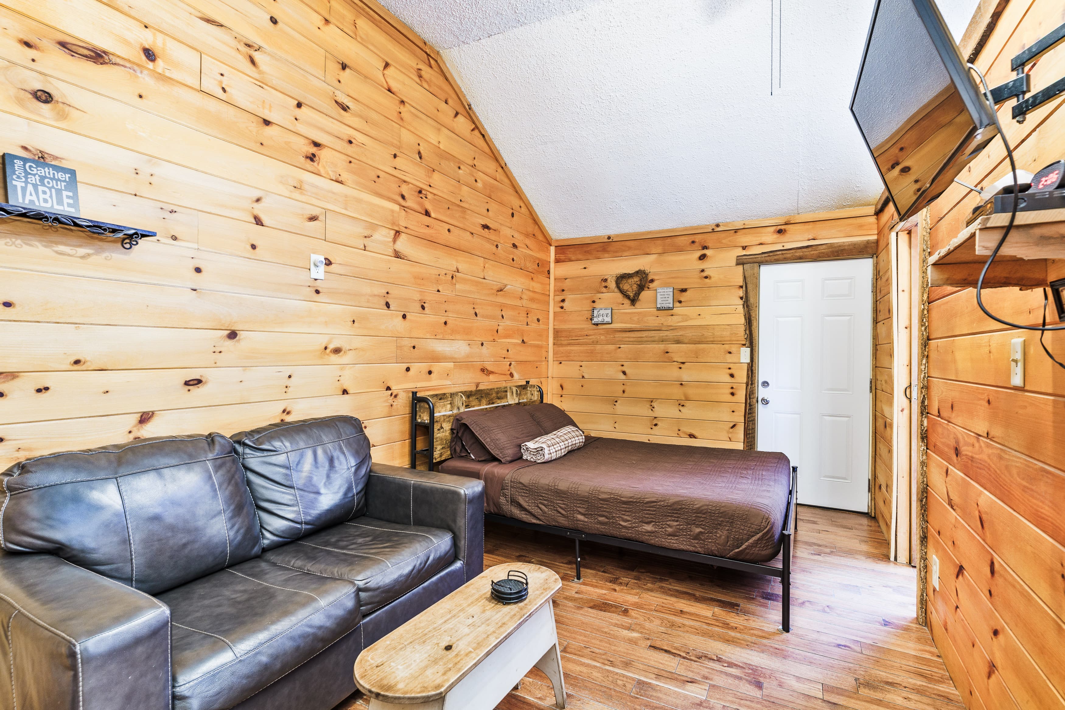 Cozy cabin interior featuring a leather sofa, a bed, and wooden walls.