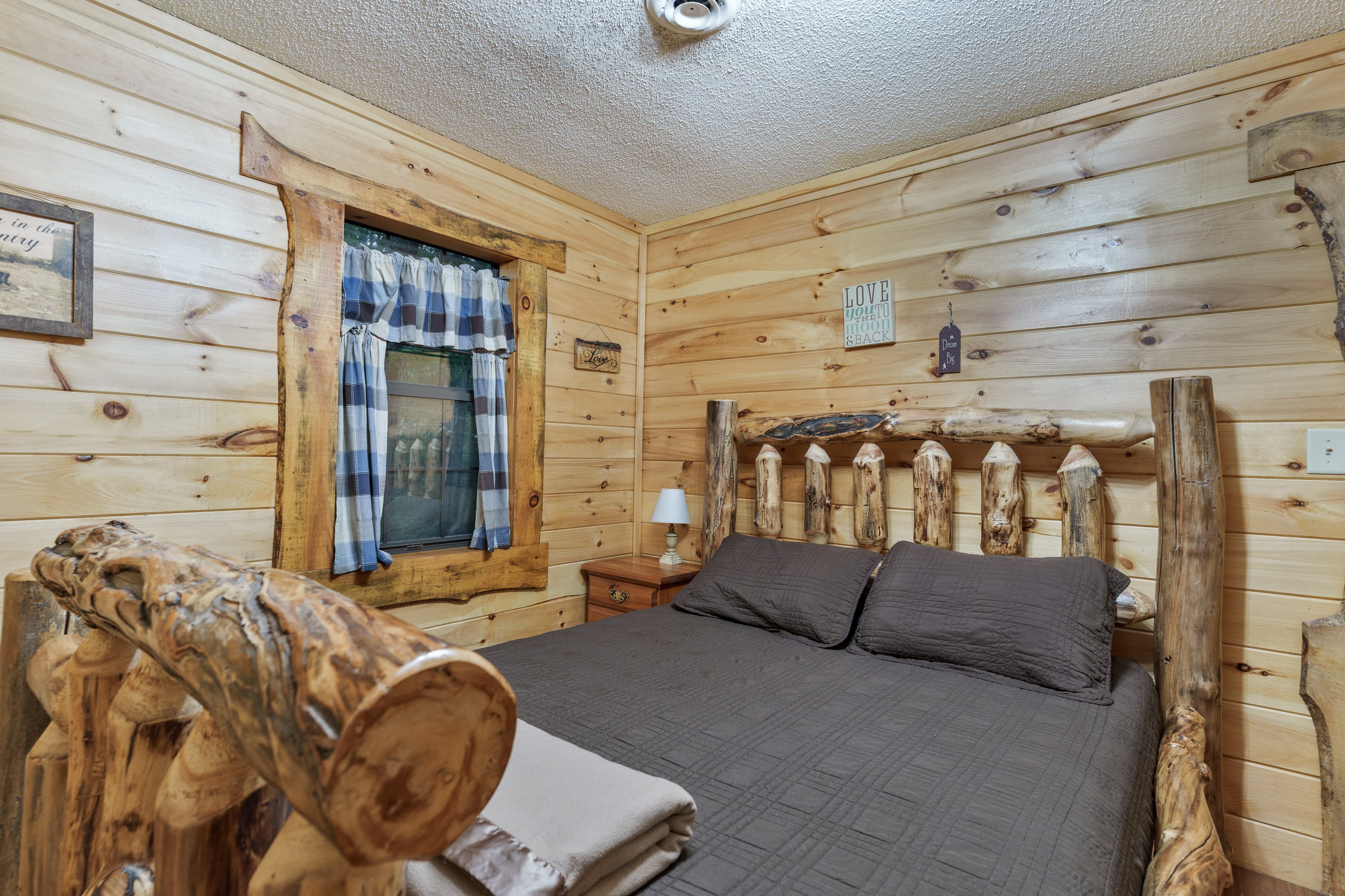 Cozy bedroom featuring a log cabin-style bed and wooden walls with a plaid curtain window.