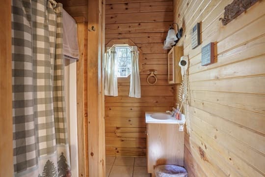 A cozy wooden bathroom featuring a shower with a checkered curtain, a sink, and rustic decor.