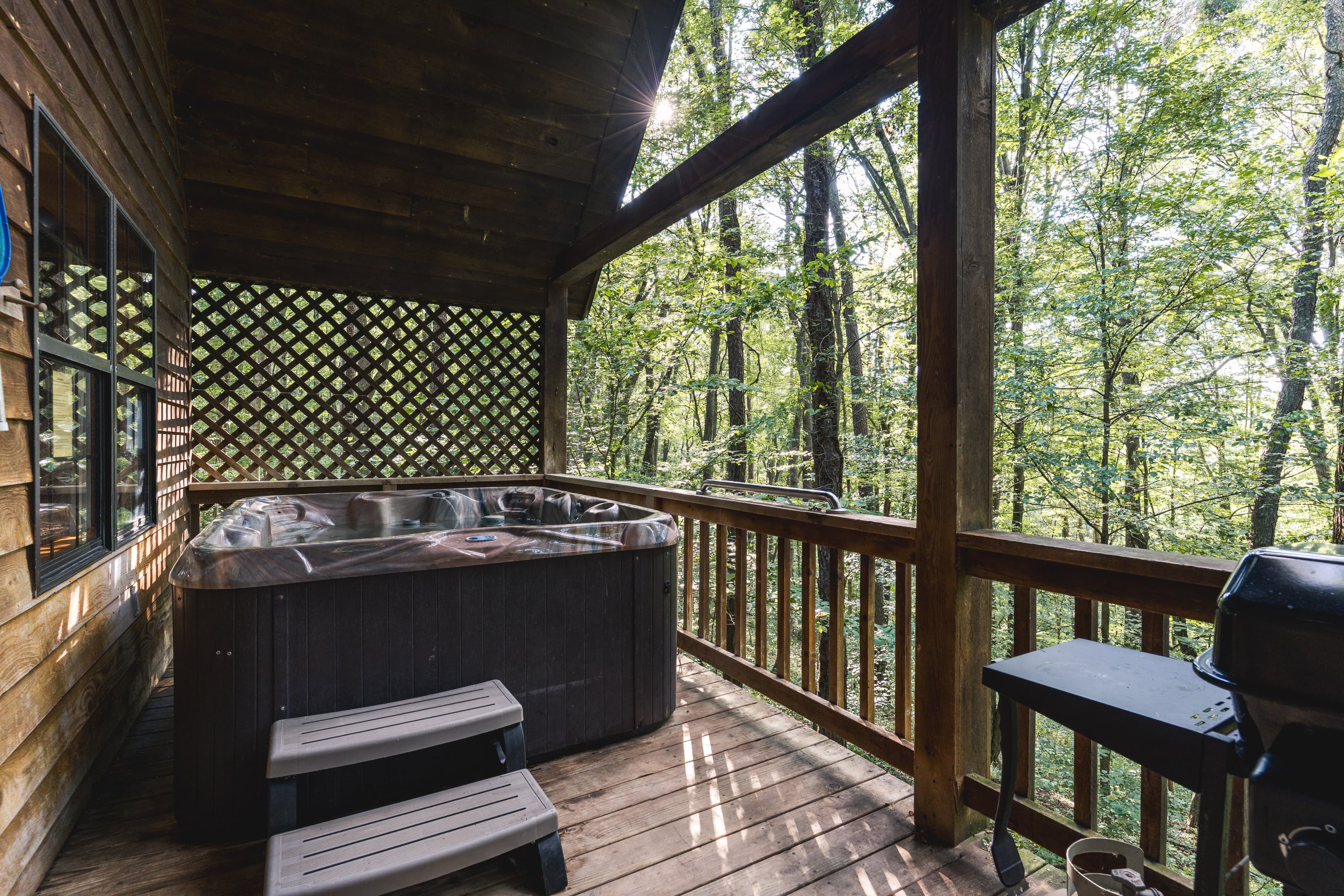 A hot tub on a wooden deck surrounded by tall trees.