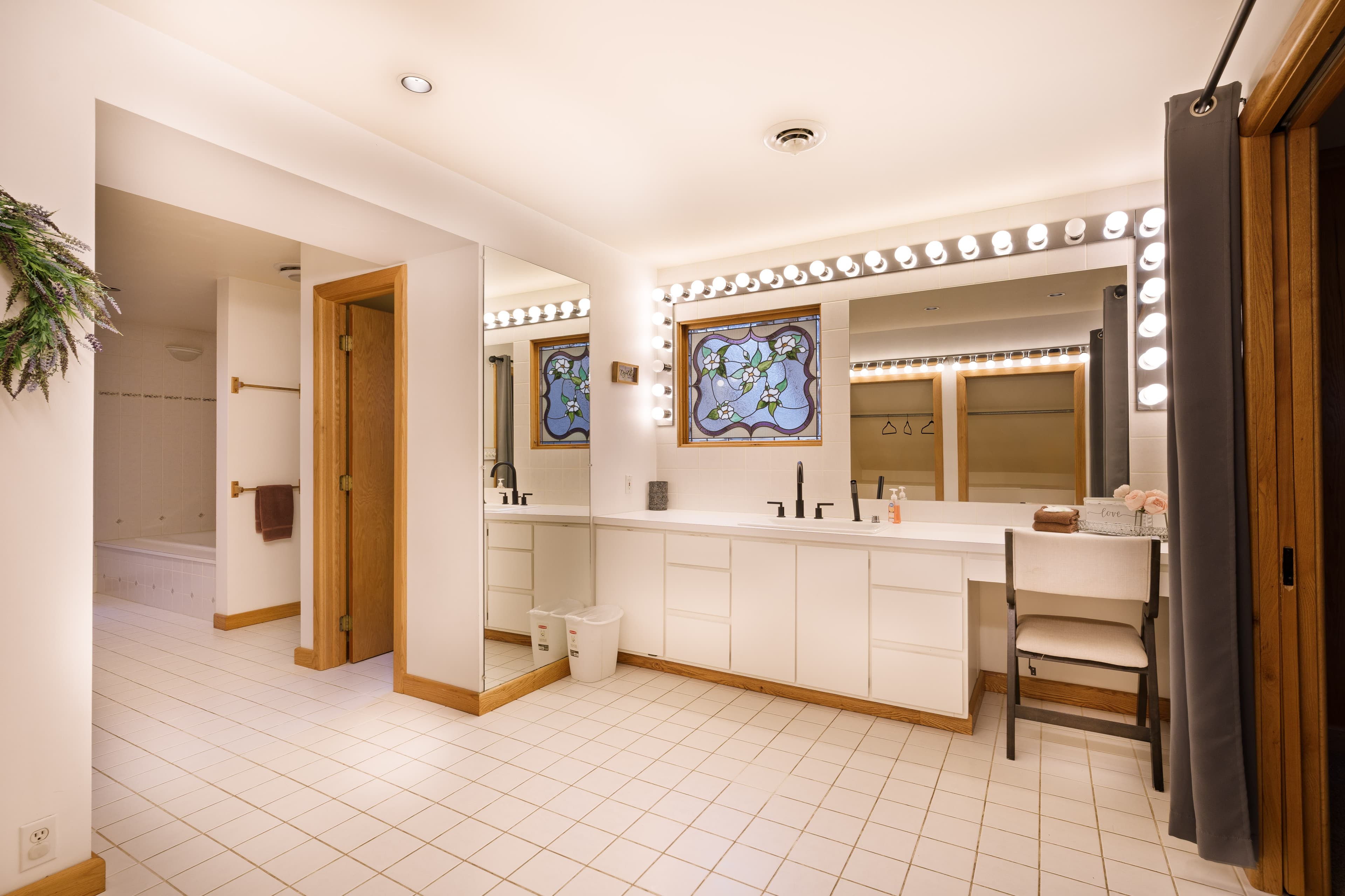 Spacious modern bathroom with a bright vanity, large mirror, and decorative stained glass window.