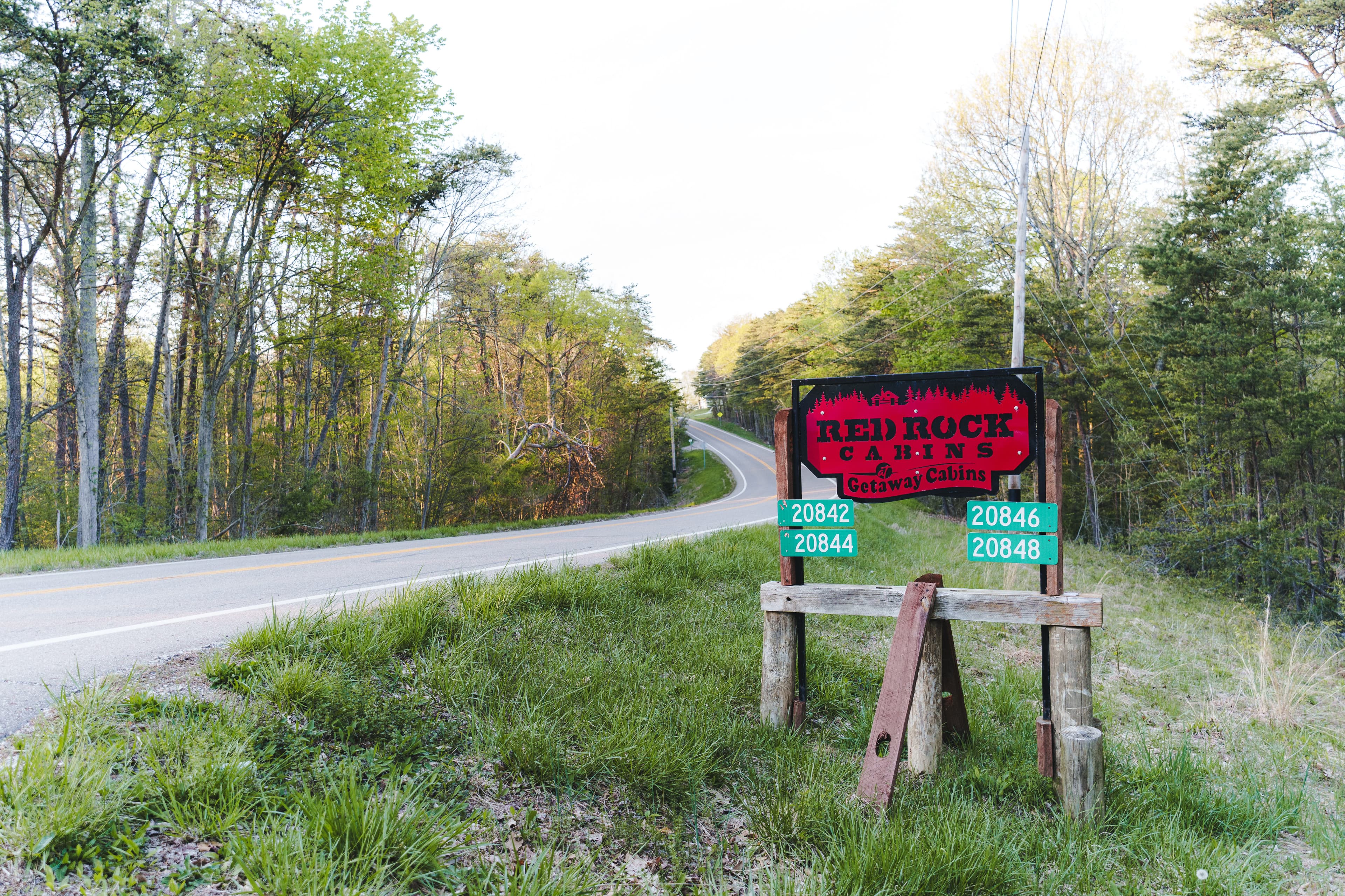 A road sign for Red Rock Cabins is posted near a winding road surrounded by trees.