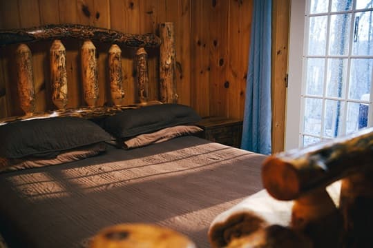 A cozy rustic bedroom featuring a wooden bed frame and soft bedding, with natural light filtering through a window.