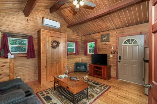Cozy wooden interior of a small living room featuring a TV, seating area, and front door.