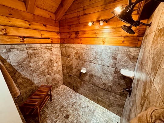 A spacious, rustic shower with wooden walls, tiled floor, and a wooden bench.