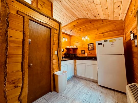 A cozy wooden kitchen featuring a white refrigerator, countertop appliances, and warm wood paneling.