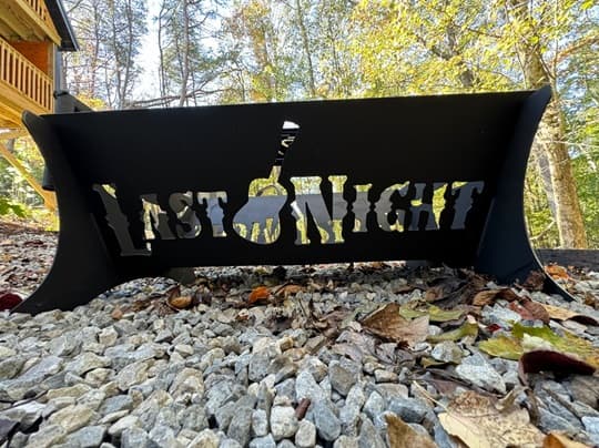 A black metal sign reading "LAST NIGHT" is set among pebbles and surrounded by autumn foliage.