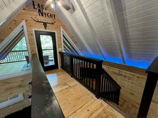 View of a rustic wooden loft with a staircase, featuring a wooden railing and blue LED lighting.