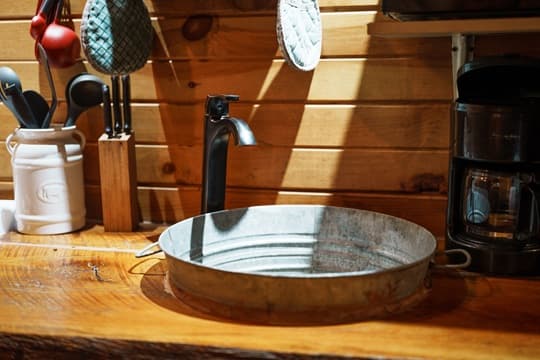 A rustic kitchen countertop featuring a metal basin, faucet, and kitchen utensils.