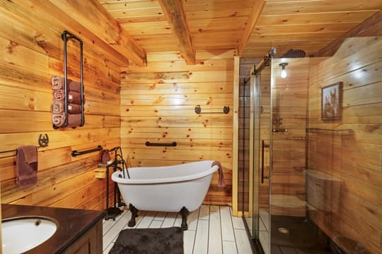 A rustic bathroom featuring a freestanding bathtub, wooden walls, and a glass shower enclosure.