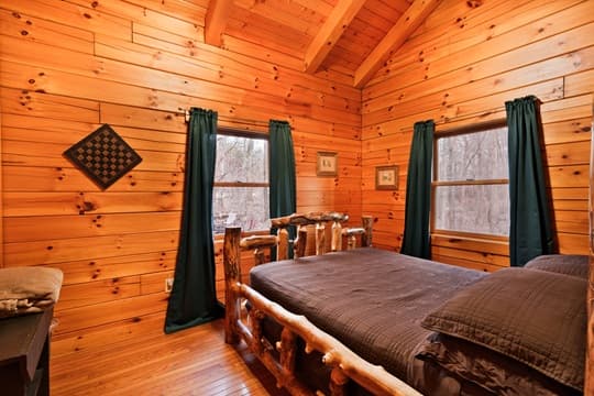 A cozy wooden bedroom with a log bed, green curtains, and natural light from two windows.