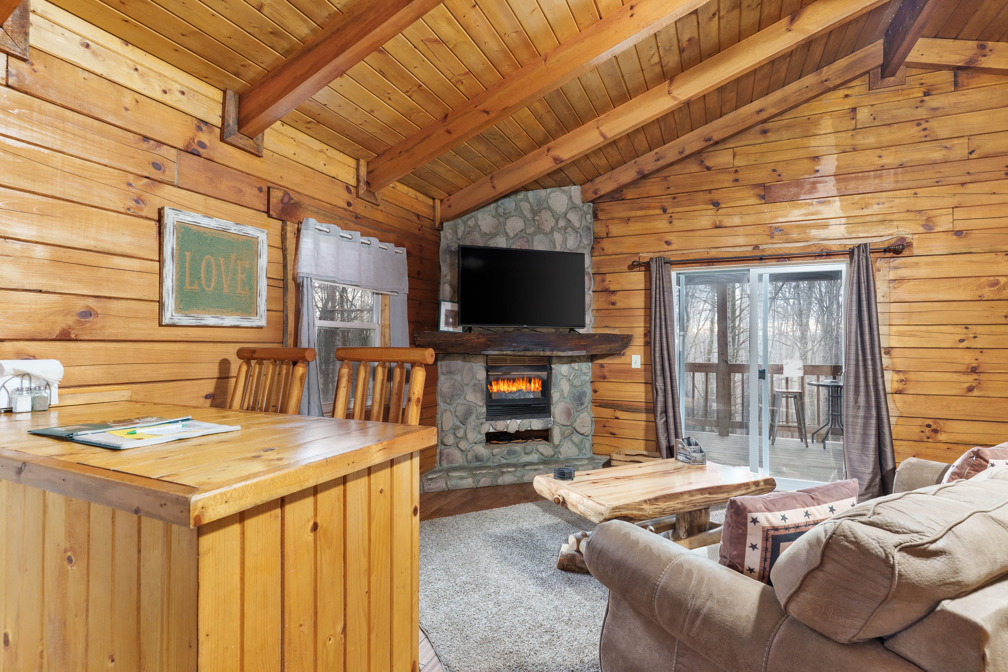 Cozy wooden cabin interior featuring a stone fireplace, TV, and large sliding doors to a deck.
