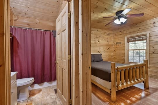 A cozy cabin interior featuring a bathroom with a shower curtain and a bedroom with a wooden bed.