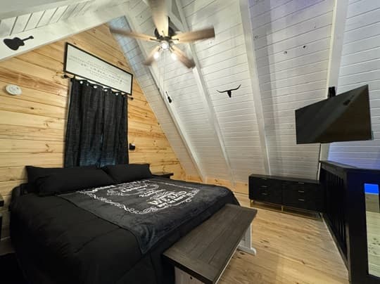 Cozy bedroom with a black bedspread, wooden walls, and a mounted television.