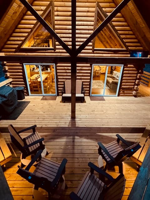 A cozy log cabin with wooden chairs arranged outside and warm light glowing from the interior.