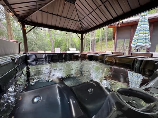 A spacious hot tub under a gazebo surrounded by trees.