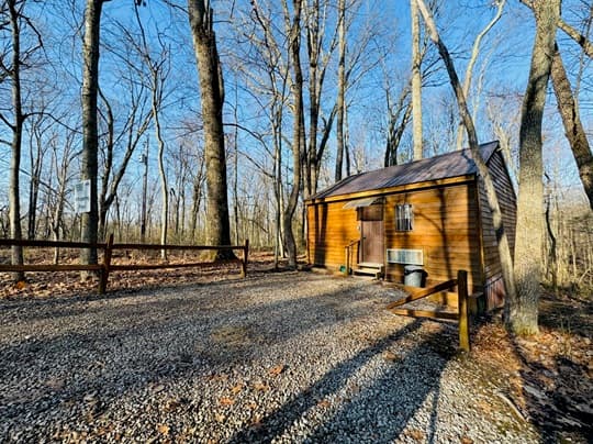 A small wooden cabin surrounded by trees on a gravel path.