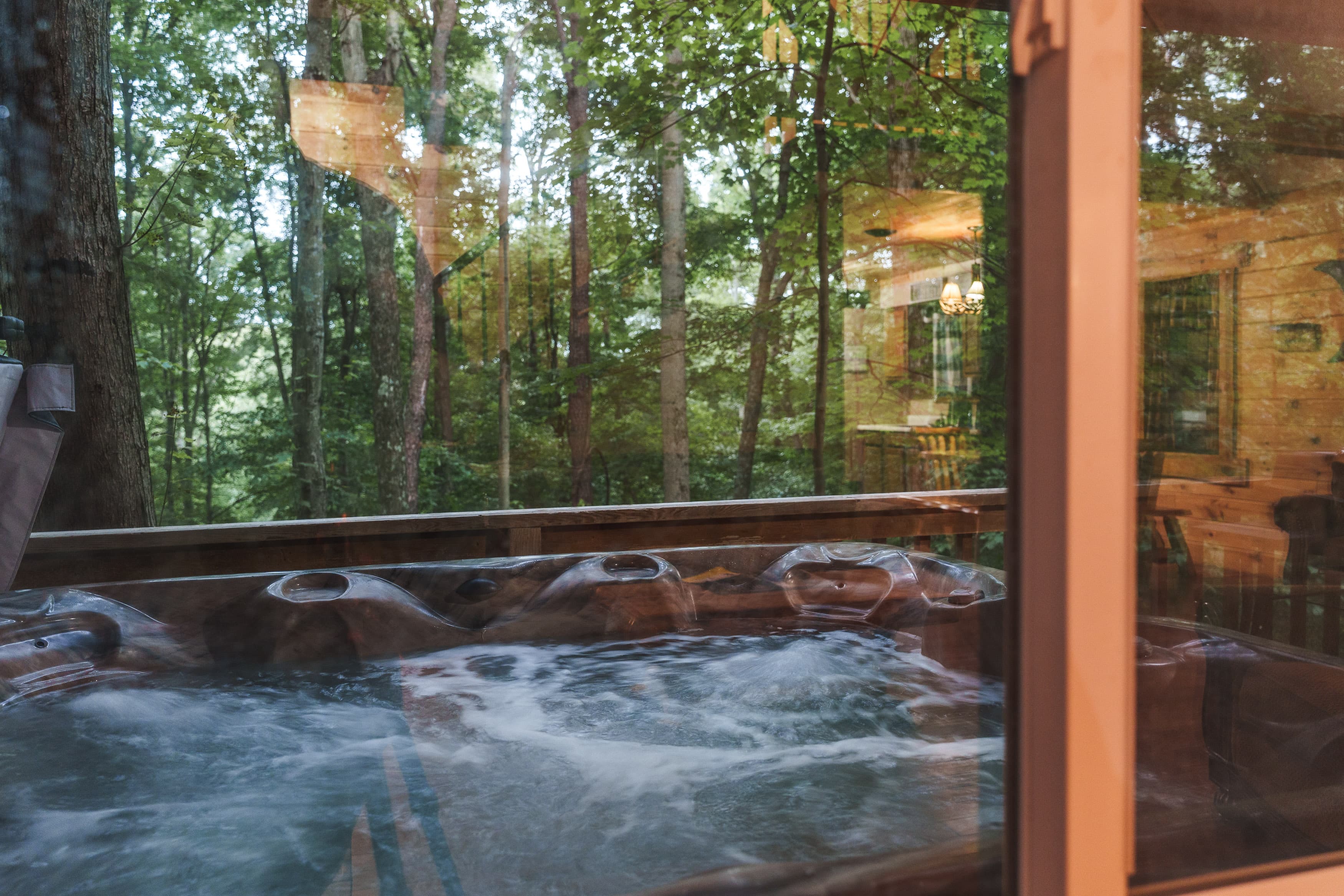 A hot tub overlooking a wooded area through a glass window.