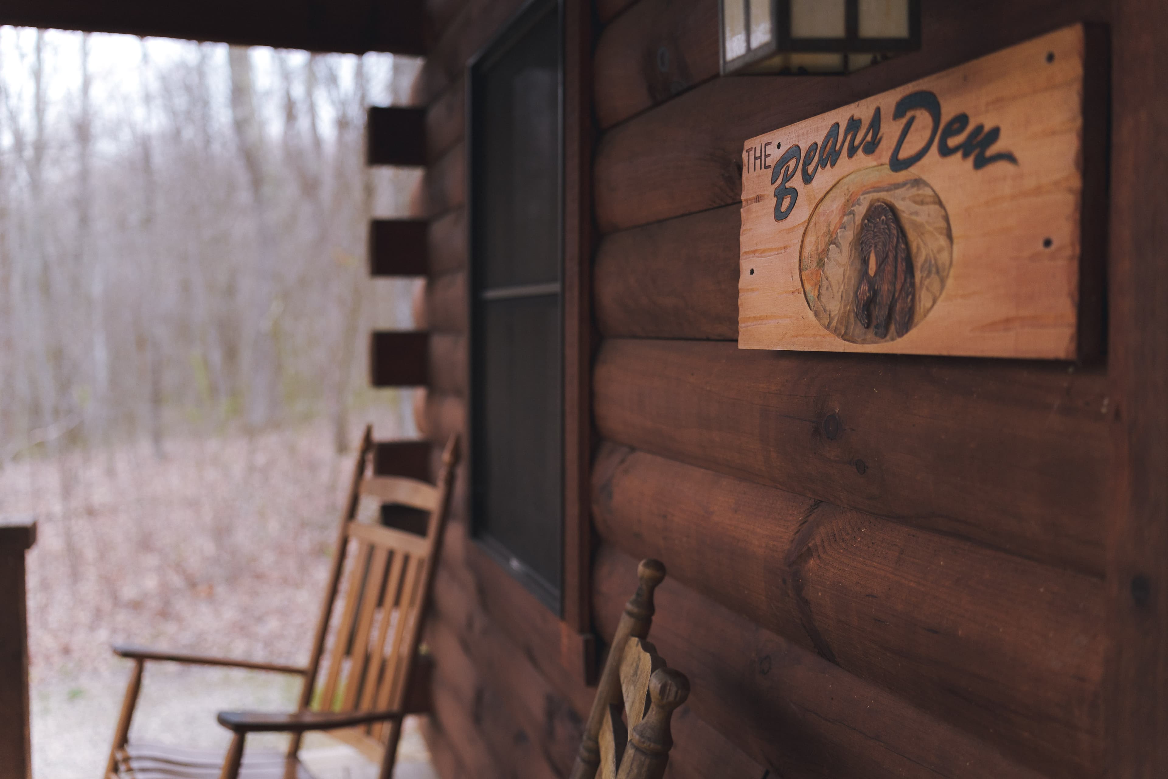 A wooden sign reading "The Bear's Den" near a rustic porch with rocking chairs.