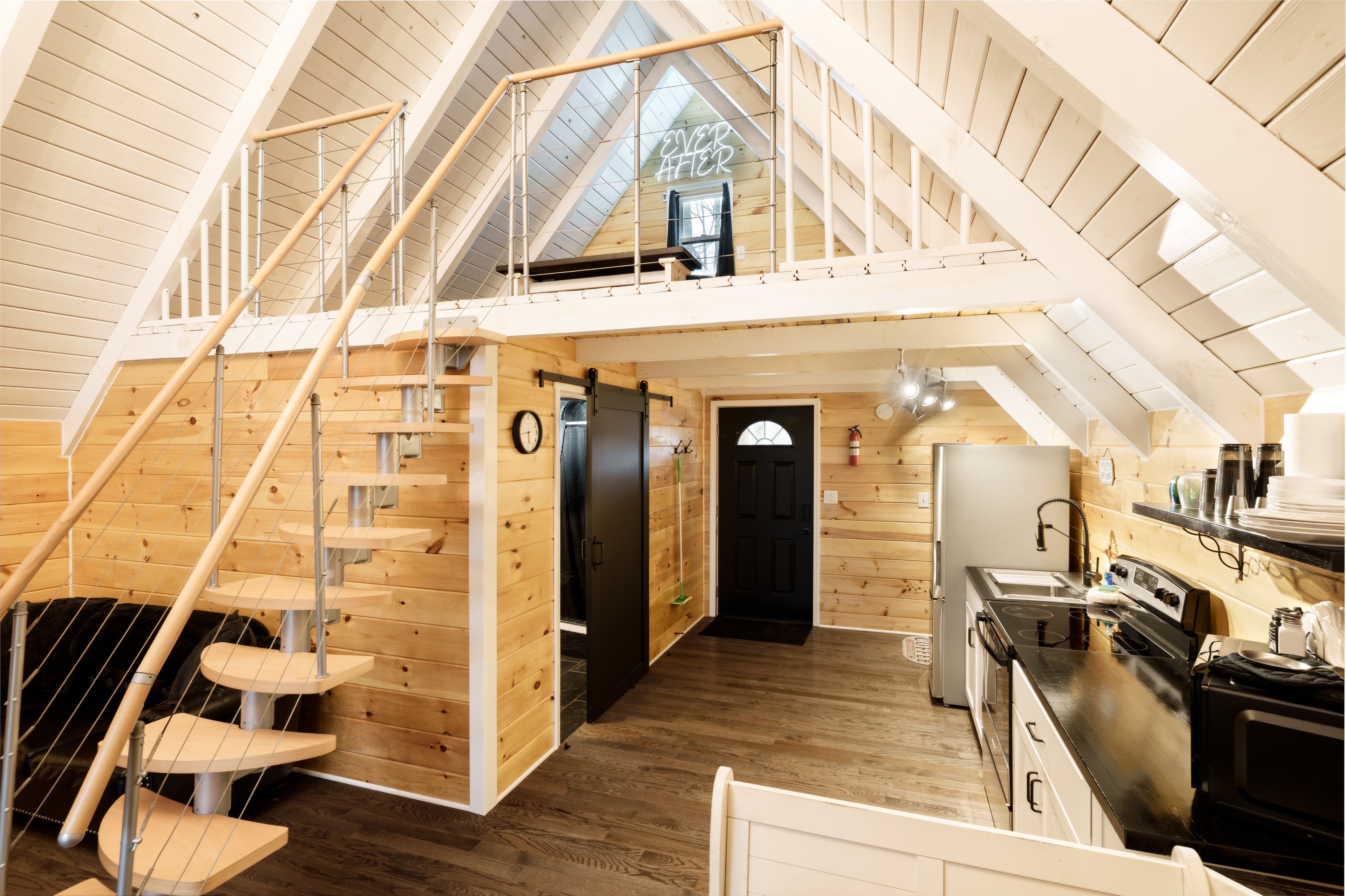 A cozy, modern loft interior with wooden walls, a spiral staircase, and an open kitchen space.