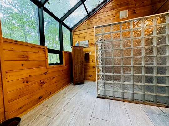 A wooden-paneled bathroom featuring a glass block shower, tiled floor, and large windows.