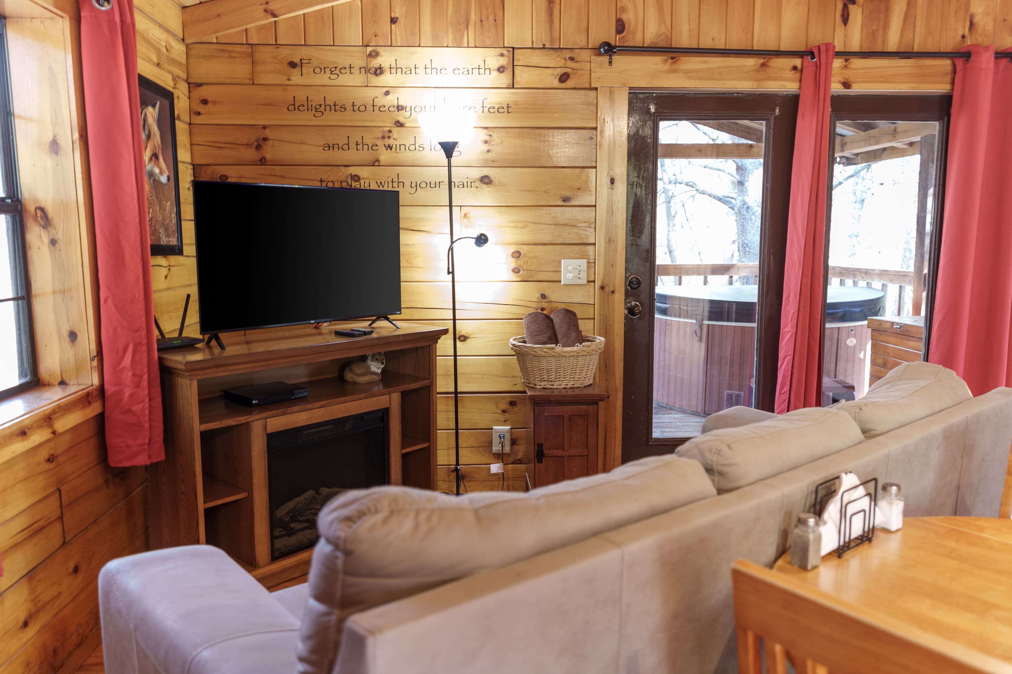 Cozy wooden cabin interior featuring a couch, TV, and door leading to a hot tub area.