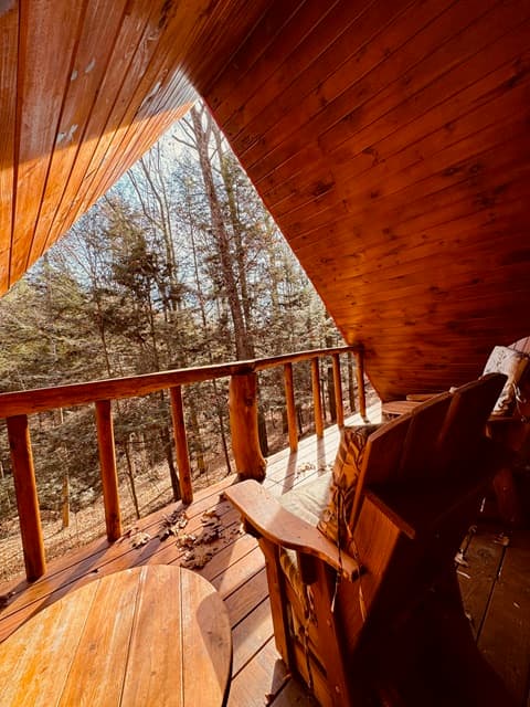 A wooden balcony overlooking a forest with a rustic chair and table.