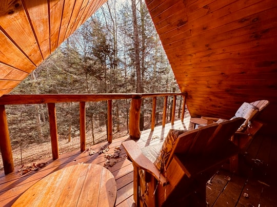A cozy wooden balcony with two chairs overlooks a forested area.