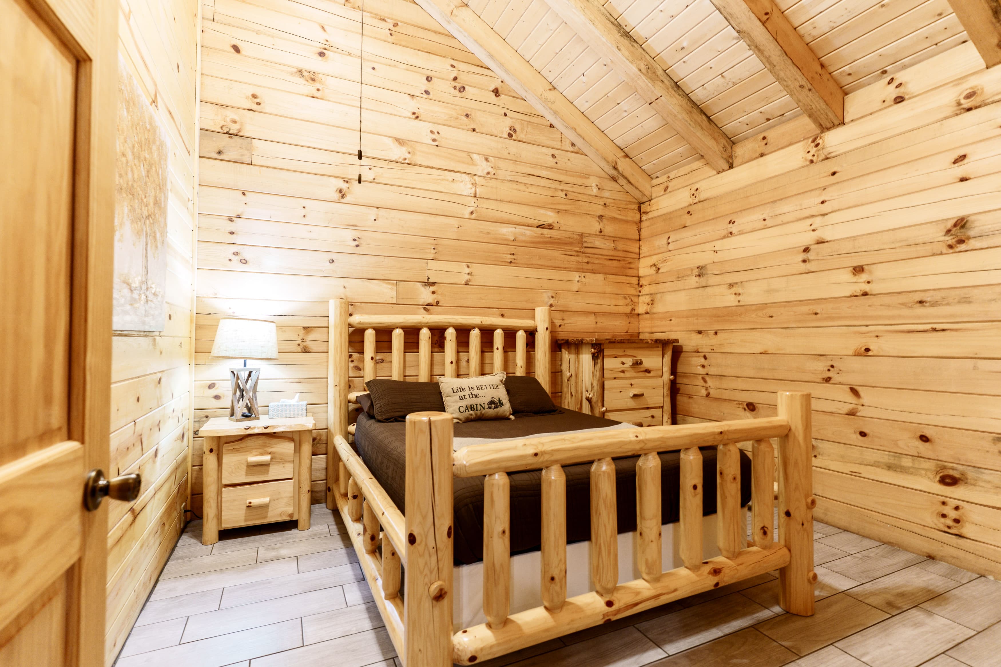 Cozy wooden cabin bedroom with a log bed, nightstand, and warm wooden walls.