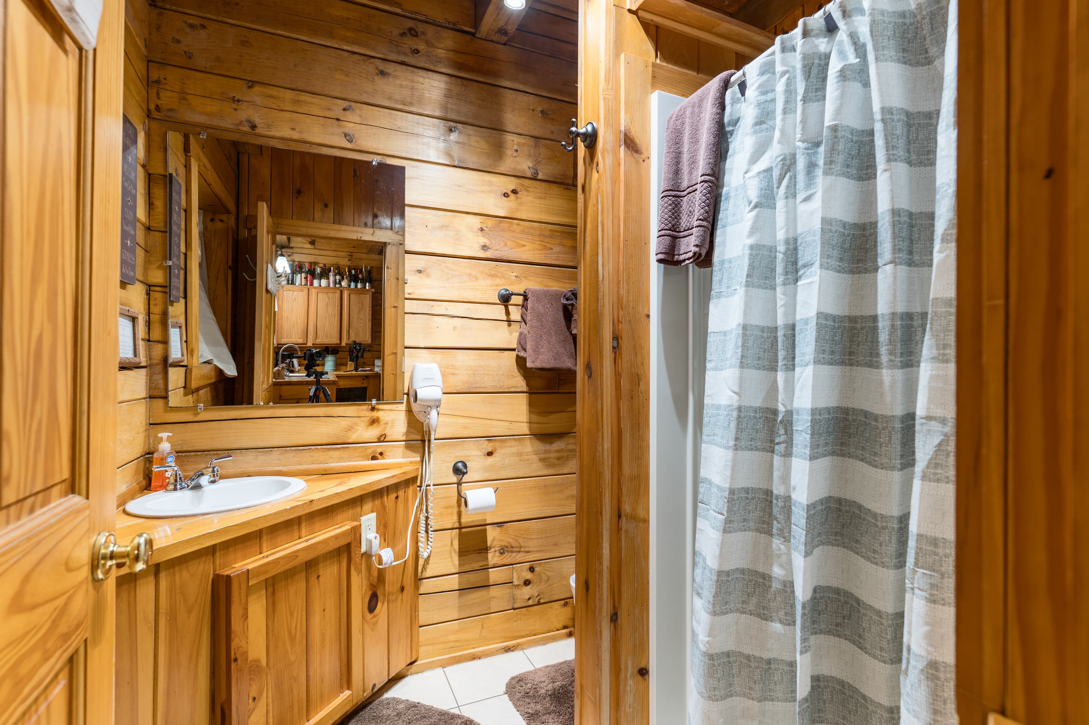A cozy wooden bathroom featuring a shower, sink, mirror, and towels.