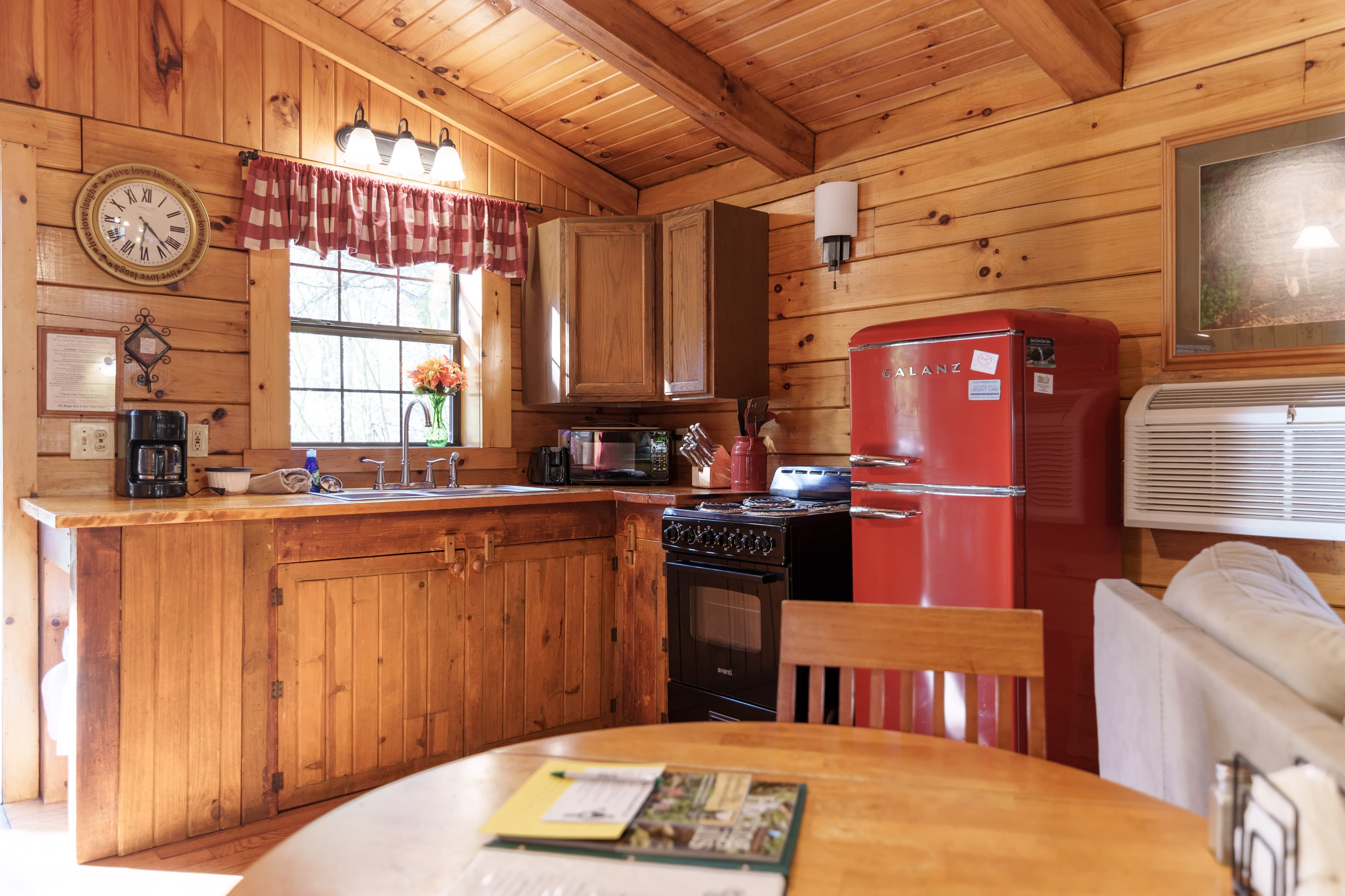 A rustic kitchen featuring wood paneling, a red refrigerator, and a round dining table.